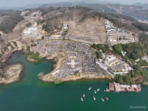 Letecký snímek na oslavu výročí církve Shincheonji. Událost se koná v parku v Cheongpyeong v Jižní Koreji. Park u pobřeží je zcela zaplněný lidmi, kteří vzdávají bohoslužbu.